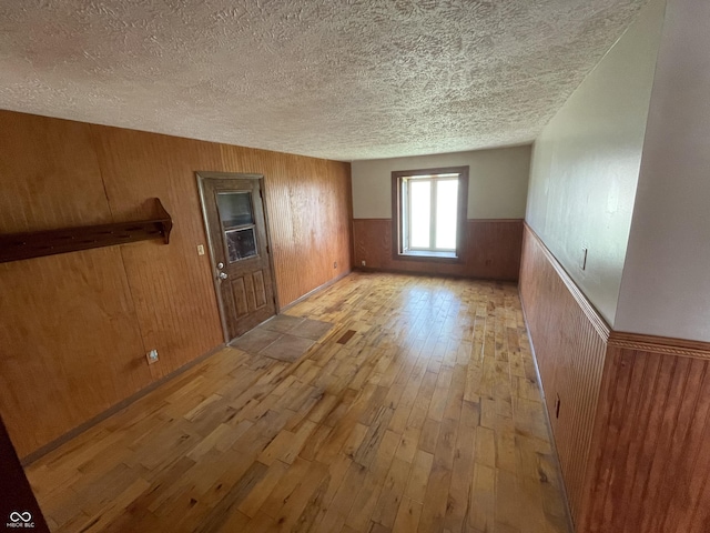 unfurnished room featuring wooden walls, a textured ceiling, light wood-style flooring, and a wainscoted wall