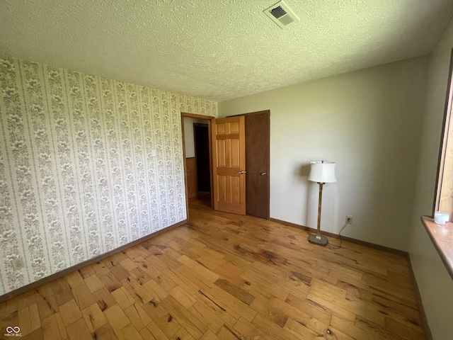 unfurnished bedroom with baseboards, wood-type flooring, a textured ceiling, and visible vents