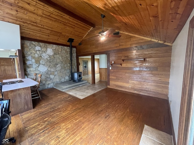 unfurnished living room featuring a wood stove, wood-type flooring, wood walls, a ceiling fan, and wood ceiling