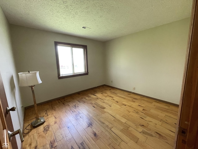 spare room with a textured ceiling, visible vents, baseboards, and light wood finished floors