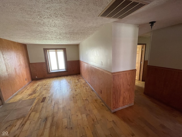unfurnished room featuring a wainscoted wall, hardwood / wood-style flooring, wood walls, and a textured ceiling