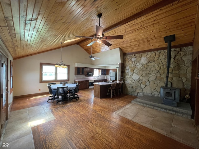 living room with baseboards, ceiling fan, wood ceiling, and a wood stove