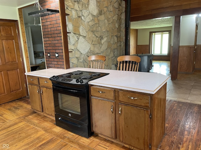 kitchen with light countertops, electric range, brown cabinetry, and a wainscoted wall