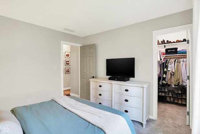 bedroom with light carpet, a walk in closet, baseboards, visible vents, and a closet