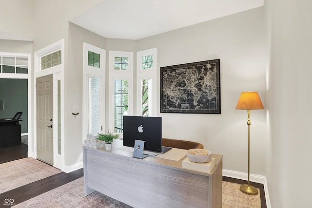 office featuring baseboards, wood finished floors, and a towering ceiling