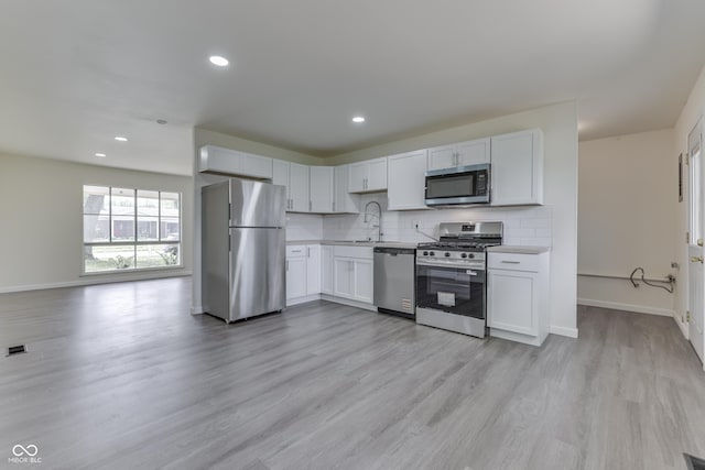 kitchen featuring baseboards, light countertops, light wood-style flooring, appliances with stainless steel finishes, and backsplash