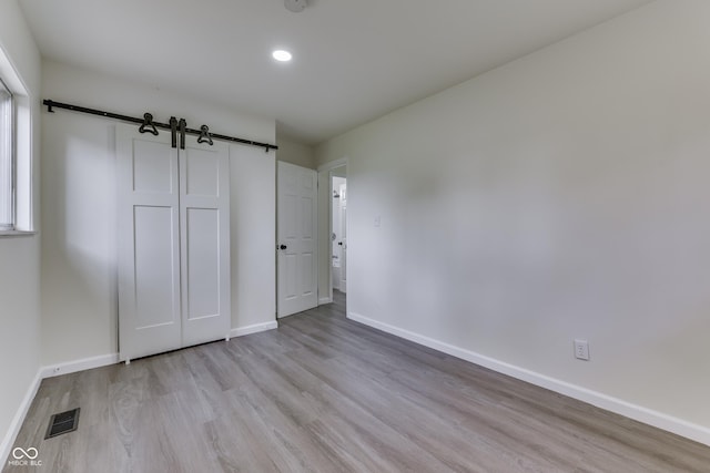 unfurnished bedroom featuring visible vents, wood finished floors, baseboards, recessed lighting, and a barn door