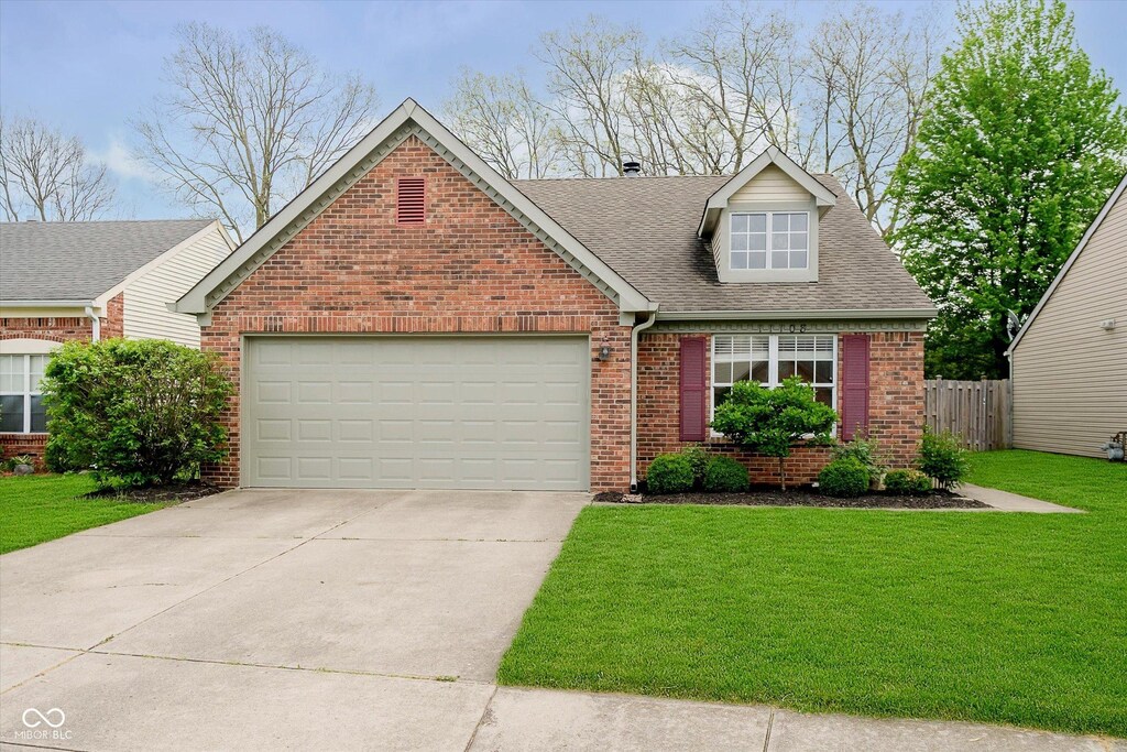 view of front of home with a garage, a front lawn, roof with shingles, brick siding, and driveway
