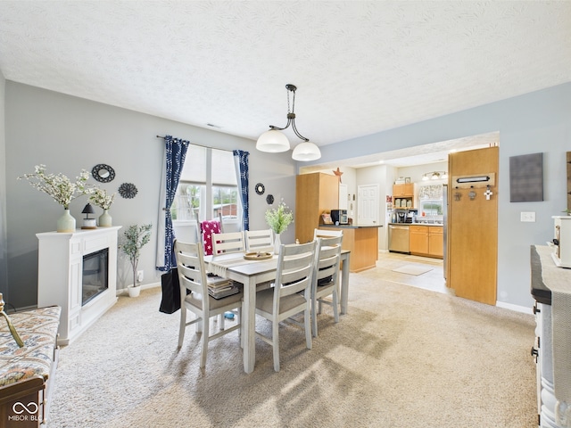 dining room featuring a glass covered fireplace, baseboards, a textured ceiling, and light colored carpet