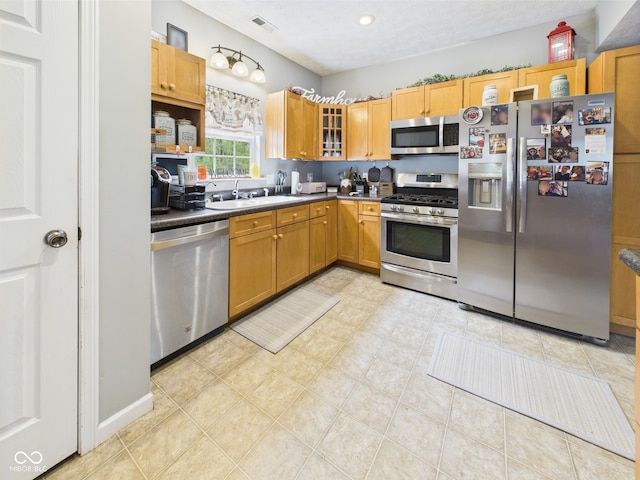kitchen featuring visible vents, dark countertops, glass insert cabinets, a sink, and stainless steel appliances