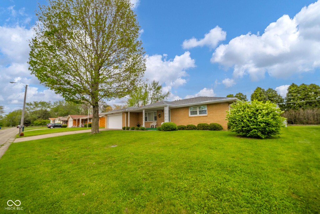 ranch-style home featuring concrete driveway, brick siding, an attached garage, and a front yard