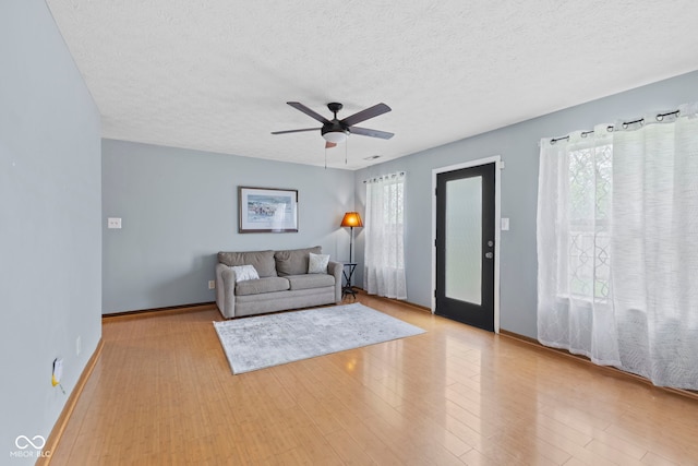 living room featuring ceiling fan, a textured ceiling, baseboards, and wood finished floors