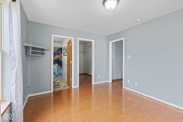 unfurnished bedroom with a textured ceiling, baseboards, wood finished floors, and a walk in closet