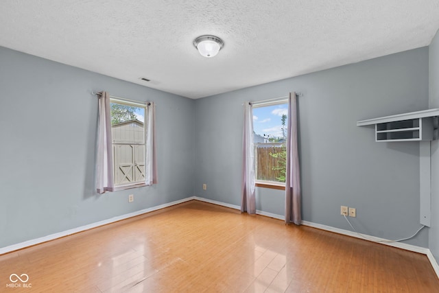 spare room with a textured ceiling, baseboards, visible vents, and wood finished floors