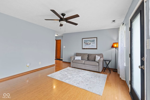 living room with light wood finished floors, baseboards, a ceiling fan, and a healthy amount of sunlight