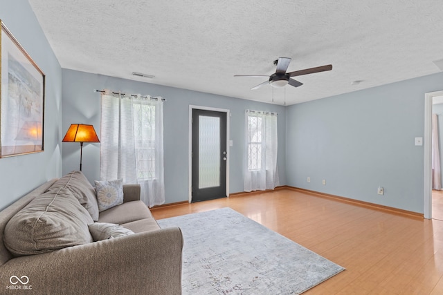 living area featuring a textured ceiling, a ceiling fan, visible vents, and wood finished floors