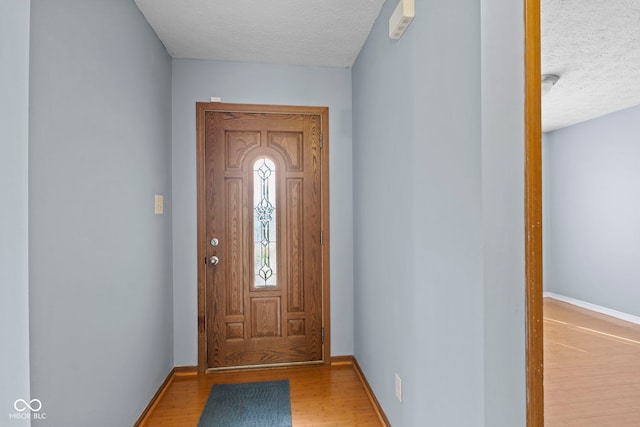 doorway to outside featuring a textured ceiling, baseboards, and wood finished floors