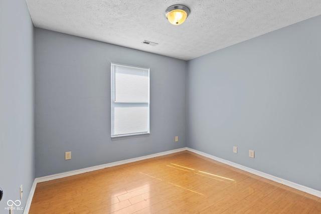 spare room featuring a textured ceiling, baseboards, visible vents, and wood finished floors