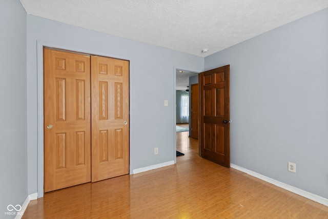 unfurnished bedroom with a closet, light wood-style floors, baseboards, and a textured ceiling