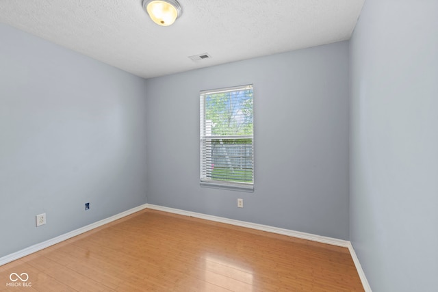unfurnished room with baseboards, light wood finished floors, visible vents, and a textured ceiling
