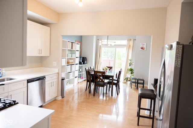 kitchen featuring light wood-type flooring, light countertops, a sink, stainless steel appliances, and white cabinetry
