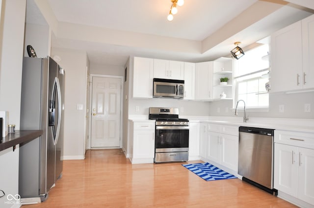 kitchen with white cabinets, stainless steel appliances, open shelves, and a sink