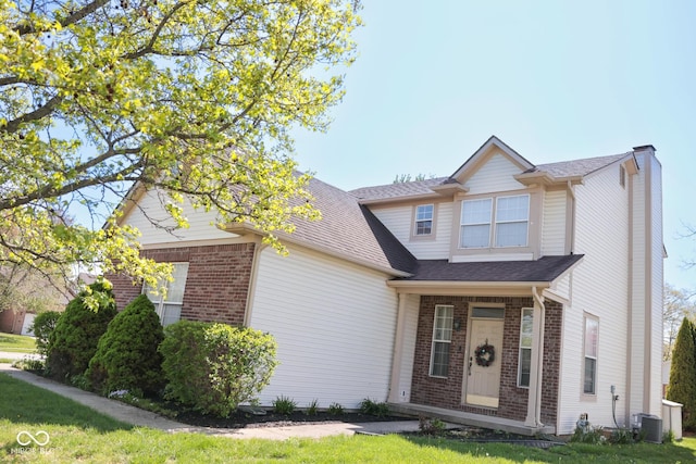 traditional-style home with a shingled roof, central AC, brick siding, a front yard, and a chimney