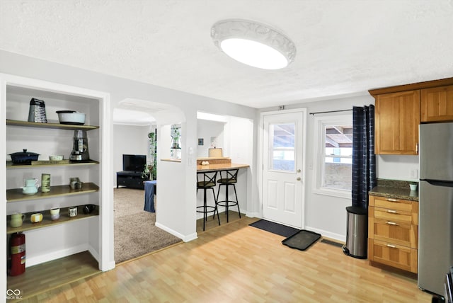 kitchen with freestanding refrigerator, arched walkways, brown cabinets, and light wood-type flooring