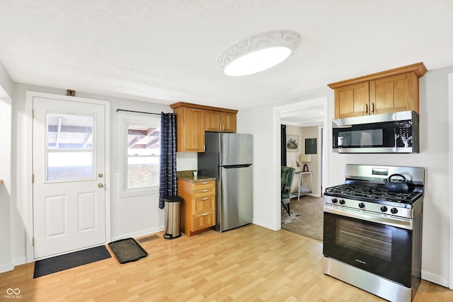 kitchen with light wood-style floors, appliances with stainless steel finishes, baseboards, and brown cabinets