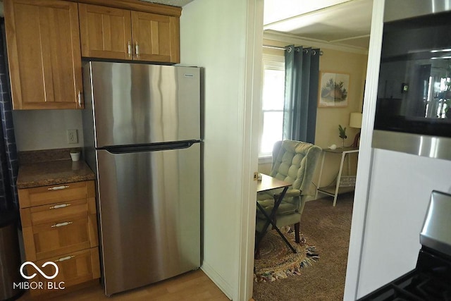 kitchen with brown cabinetry, range, crown molding, dark countertops, and freestanding refrigerator