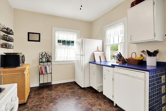 kitchen featuring white appliances, dark countertops, white cabinetry, baseboards, and stone finish flooring