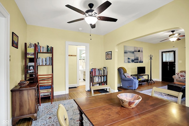 living room with a ceiling fan, wood finished floors, baseboards, and arched walkways