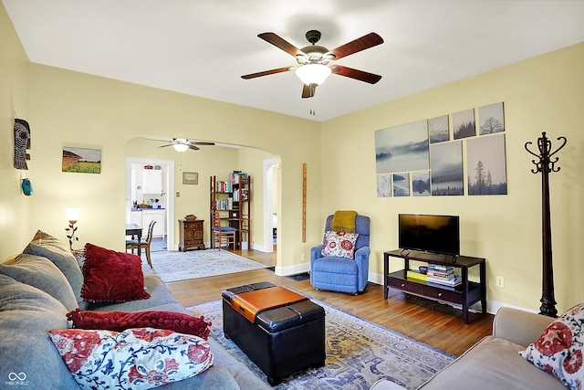 living area featuring a ceiling fan, arched walkways, wood finished floors, and baseboards