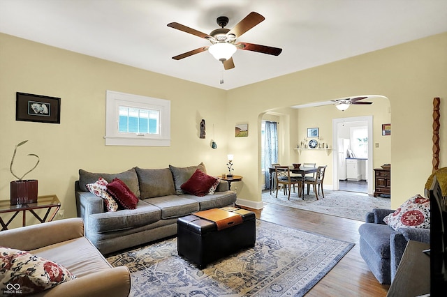 living area featuring arched walkways, a ceiling fan, and wood finished floors