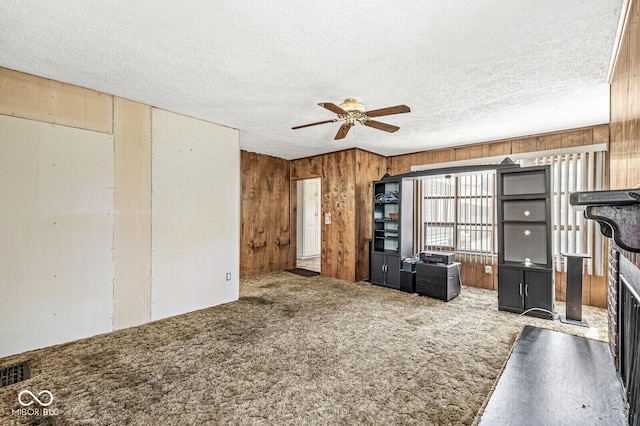 315 W High St, Pendleton, IN 46064 - unfurnished living room featuring a ceiling fan, carpet, wood walls, a fireplace, and a textured ceiling