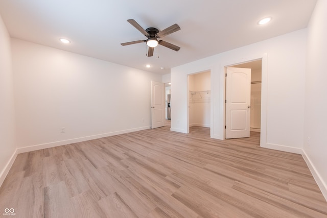 unfurnished bedroom with baseboards, a spacious closet, light wood-style flooring, and recessed lighting