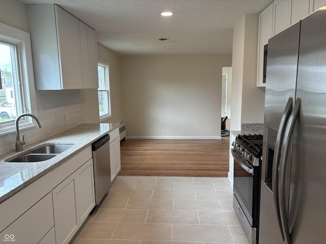 kitchen featuring appliances with stainless steel finishes, a sink, baseboards, light tile patterned floors, and light stone counters