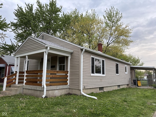 view of side of property featuring fence, covered porch, a chimney, a lawn, and a carport