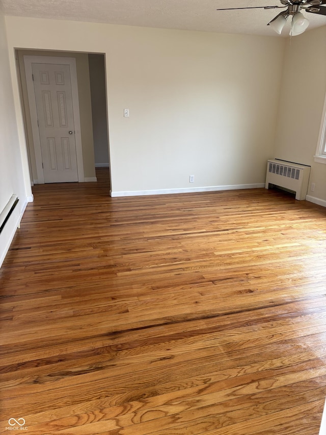 empty room with light wood-style floors, radiator, baseboards, and a ceiling fan