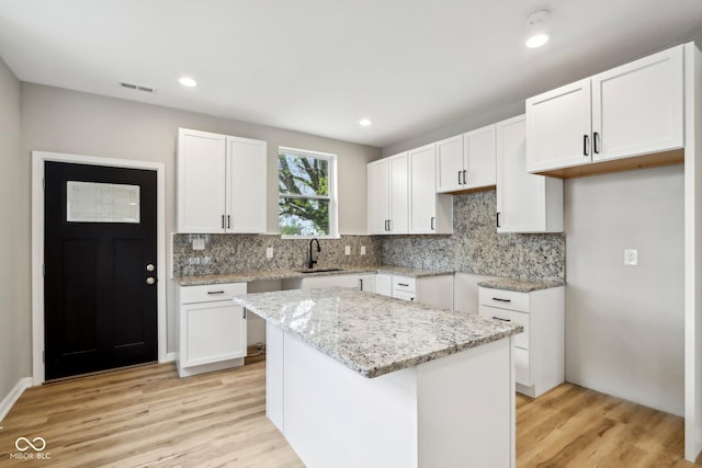 202 Mckim Ave, Indianapolis, IN 46201 - kitchen featuring light stone counters, a sink, white cabinets, light wood-style floors, and tasteful backsplash