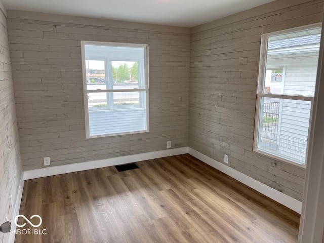 empty room with a wealth of natural light, baseboards, visible vents, and wood finished floors