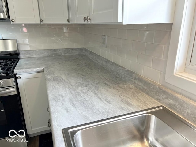 kitchen featuring stainless steel appliances, a sink, backsplash, light countertops, and white cabinets
