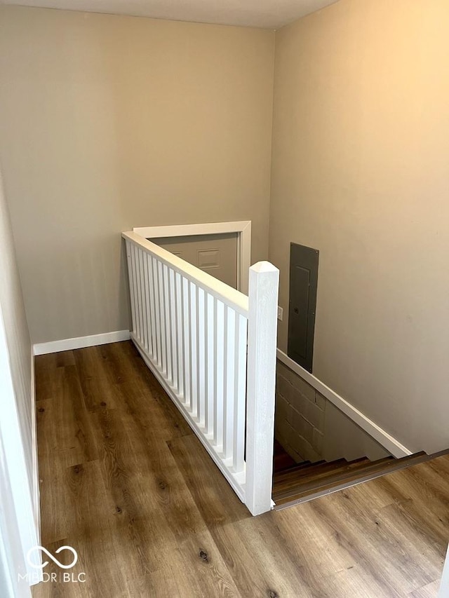 staircase with baseboards, electric panel, and wood finished floors