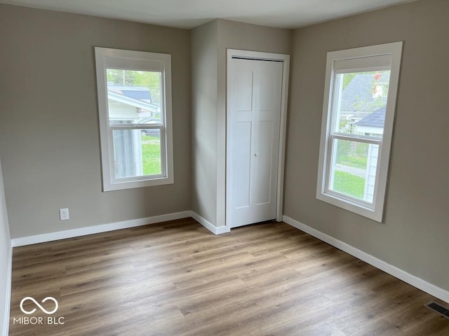 unfurnished bedroom with baseboards, multiple windows, and light wood-type flooring