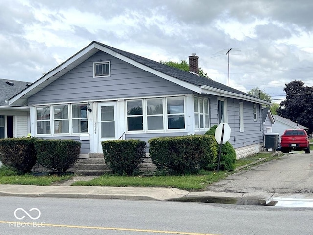 bungalow with a chimney, entry steps, cooling unit, and a shingled roof