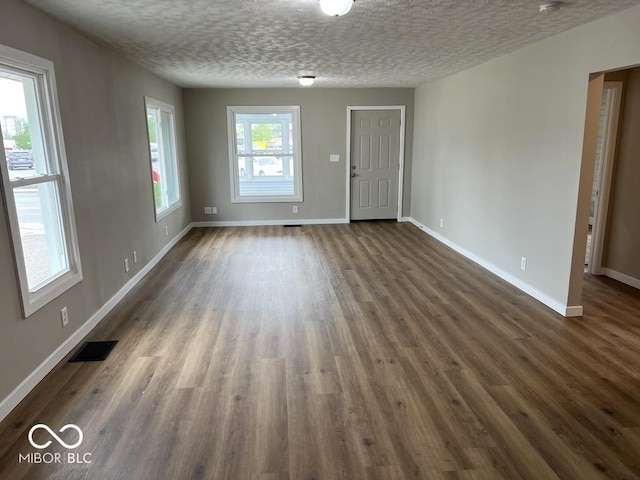 unfurnished living room featuring baseboards, dark wood finished floors, visible vents, and a textured ceiling