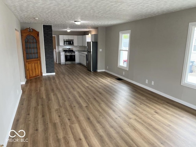 unfurnished living room featuring baseboards, dark wood-style flooring, visible vents, and a textured ceiling