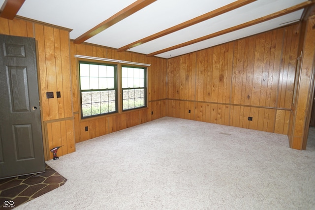 carpeted spare room featuring wooden walls and beamed ceiling