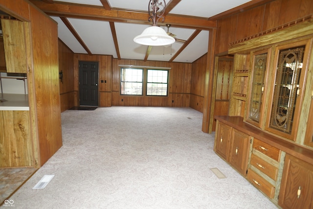 empty room featuring light colored carpet, lofted ceiling with beams, and wooden walls