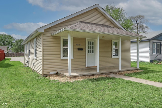bungalow-style home with covered porch, fence, a shingled roof, and a front yard